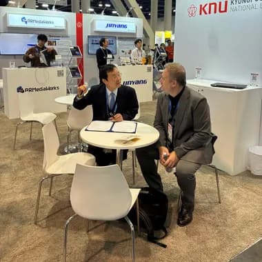 Two people in conversation across a table at an exhibition stand on a trade show floor